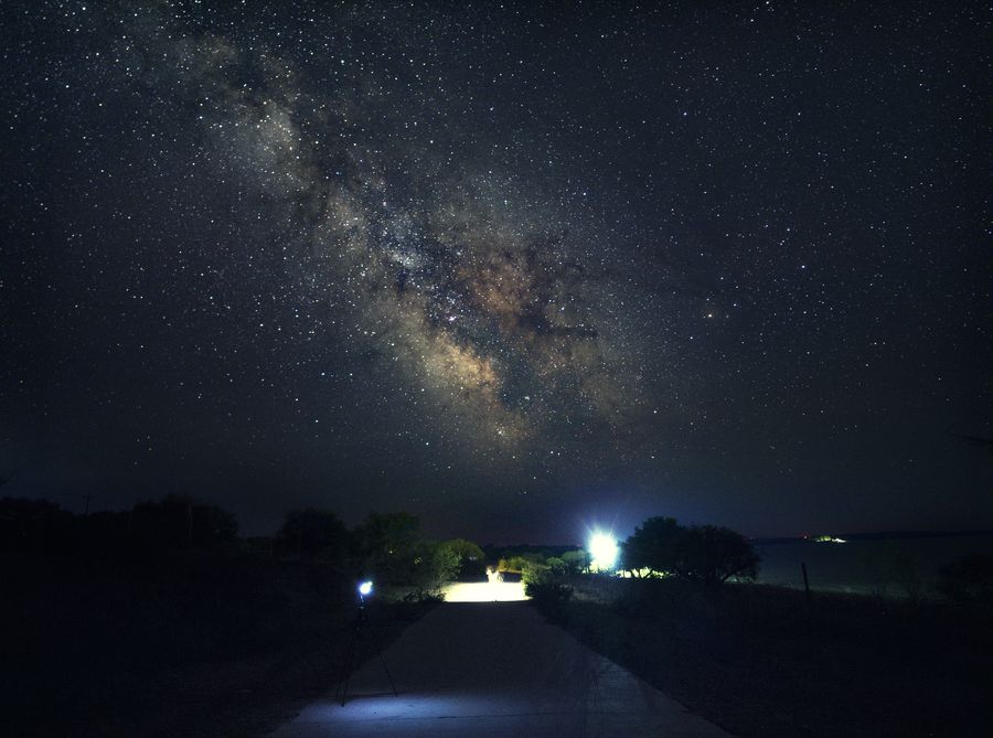向海自然保护区的银河自地平线升起，远处有零星的灯光，低空泛着淡淡的光晕