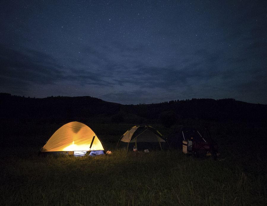 夜色里的营地，一顶帐篷透出暖黄的灯光，旁边还搭着两顶帐篷，天空是深蓝的星夜