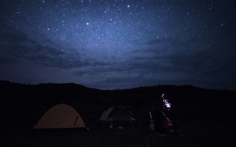 两顶帐篷扎在星空下，一个人戴着照明头灯站在中间，天空是深蓝的星夜