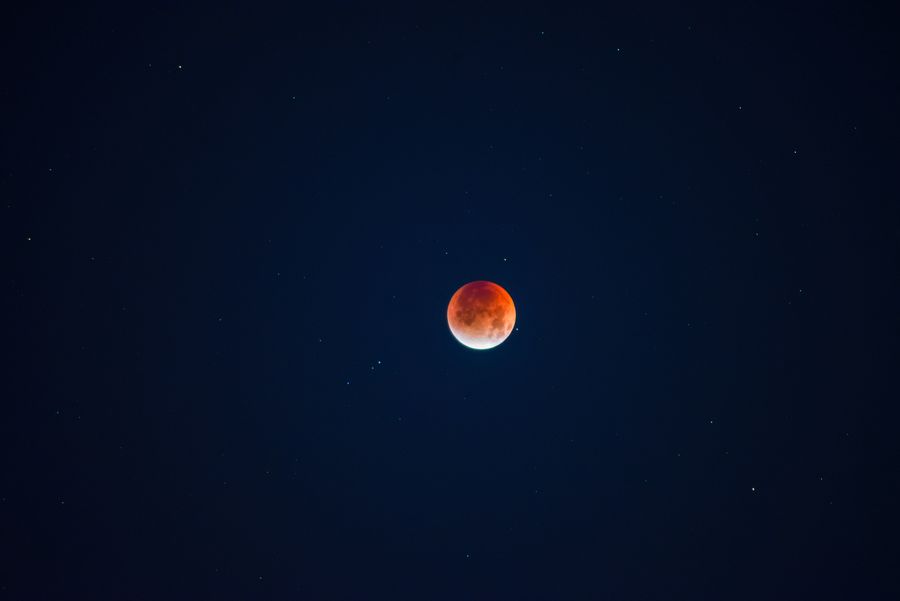 伊通河畔的夜空，一枚暗红的月亮悬在画面中间，四周散着稀疏的星点，月面下缘留着一道明亮的边缘