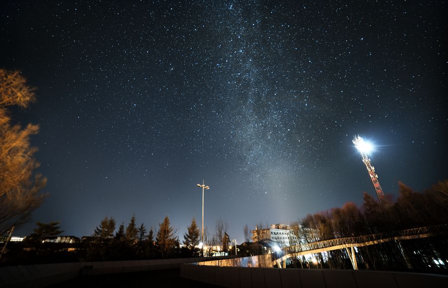二道白河镇的夜空，银河从屋舍与路灯上方升起，云层被灯光照出轮廓