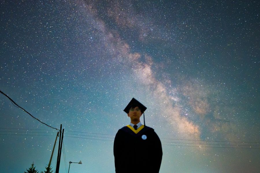 毕业生站在画面中央，身后是横贯天空的银河，人物被夜色压成剪影
