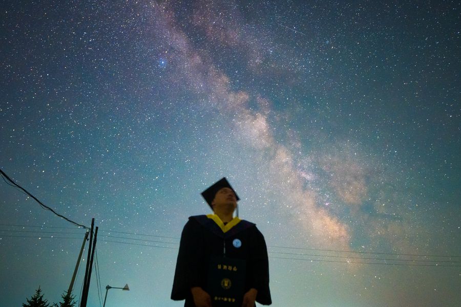 毕业生的学位帽与披肩在星空前显出轮廓，右侧是屋脊与电杆的剪影