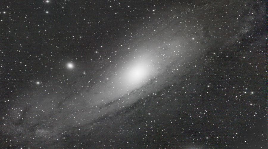 单色处理的仙女座星系，明亮的核球与盘面斜跨画面，外围散布着星点