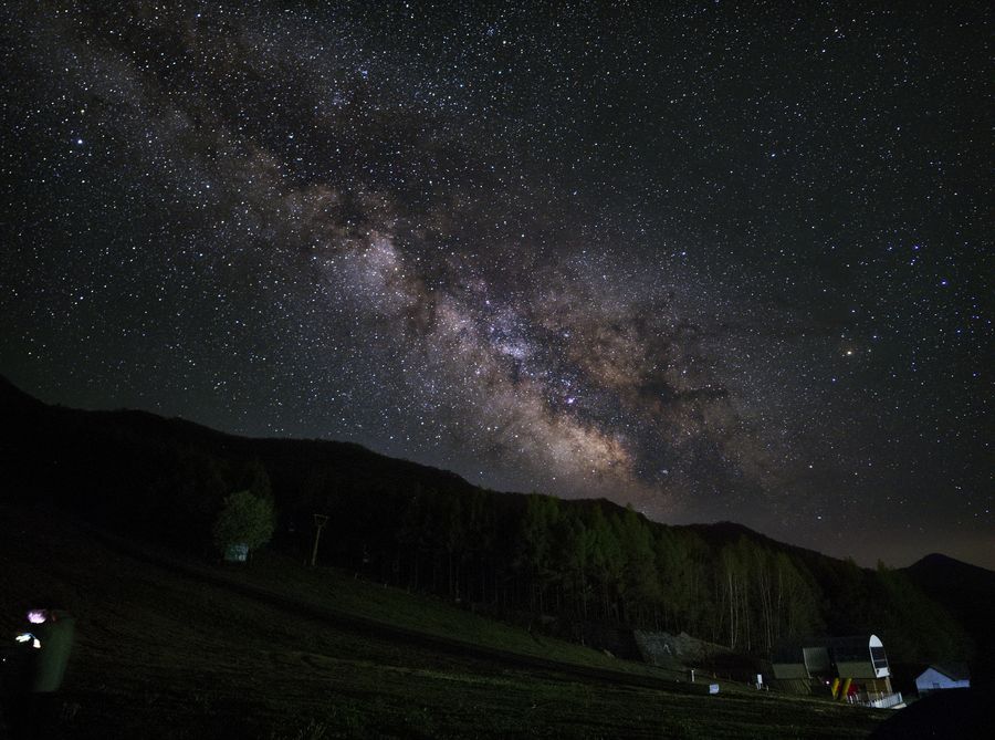 官马莲花山营地，银河斜贯天空，下方是亮着灯的观测房