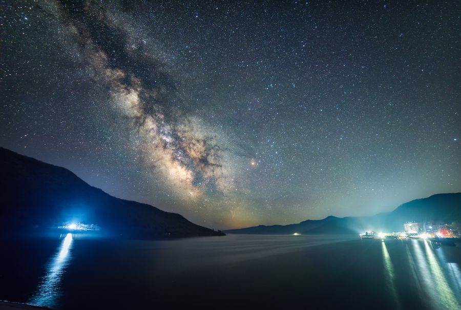 星星哨水库的夜空，银河横跨天际，水面倒映着岸边的蓝色灯光