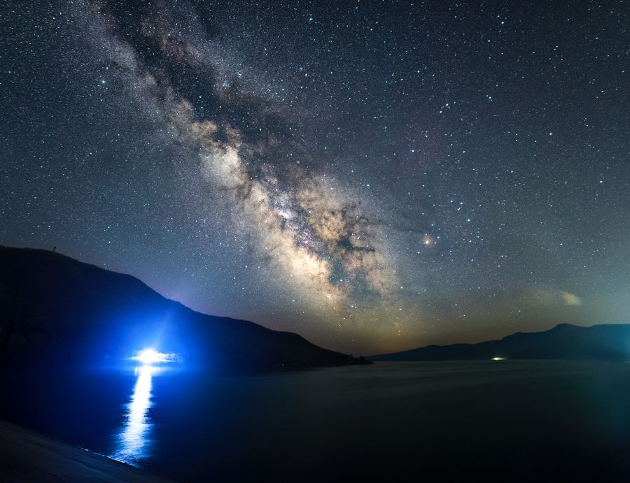 星星哨水库的水面与银河，岸边有蓝色灯光照射