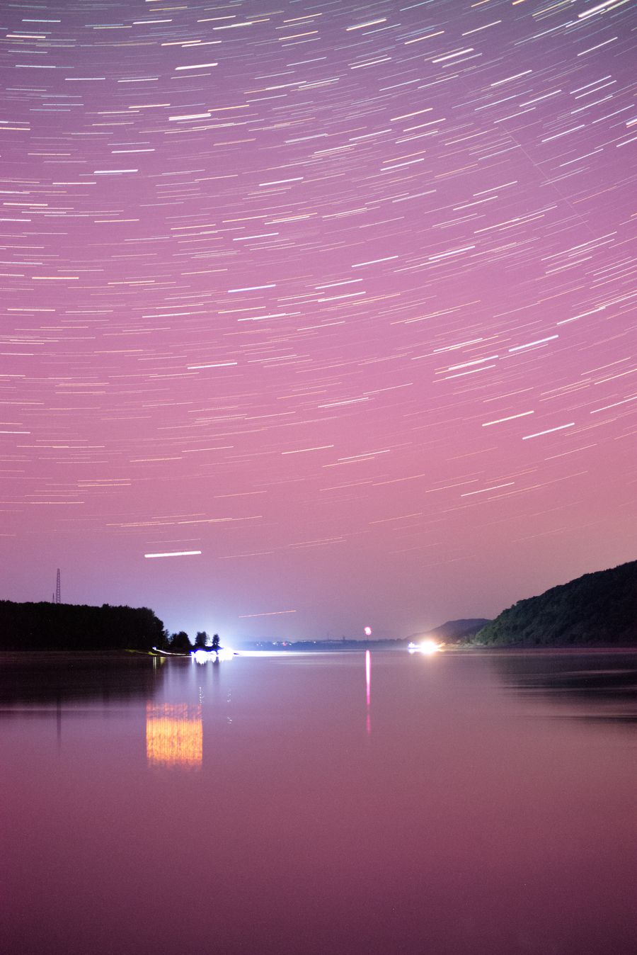 竖幅画面里，星轨绕着天极在水面上方划出弧线，江心有一盏灯